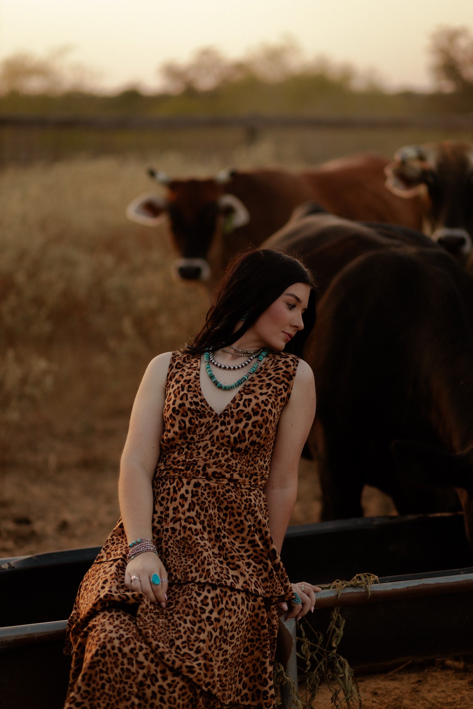 Brooke Wilhelm in a leopard dress layered with turquoise and Navajo pearl necklaces, cattle behind her